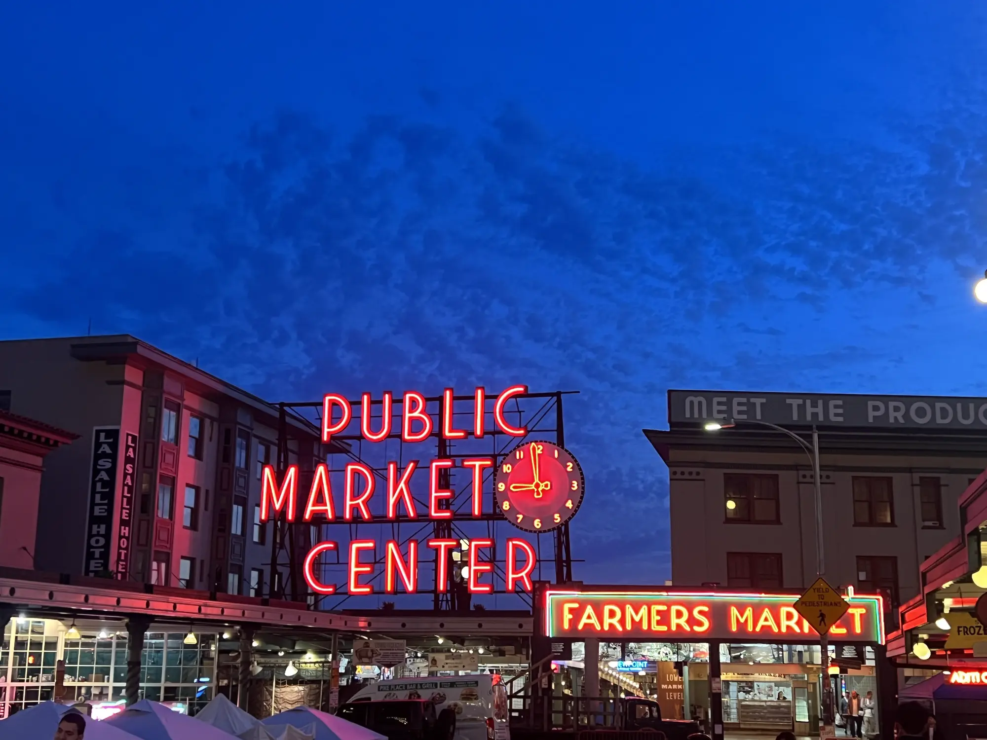Pike Place Market stalls — produce vendors, flower stands, and the central arcade where the six picks below are scattered